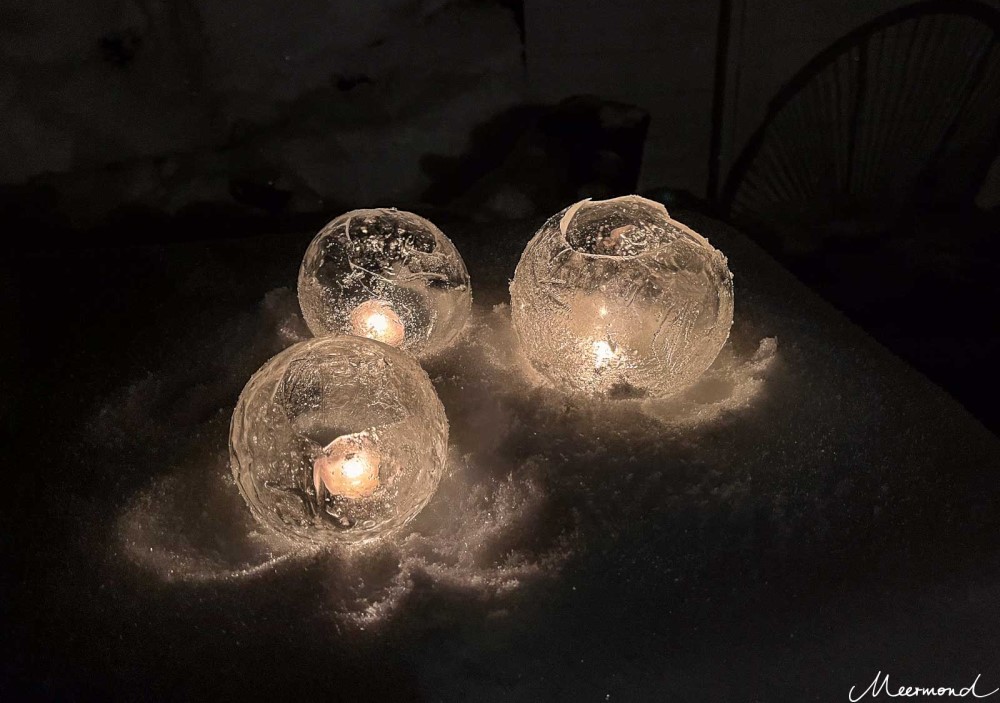 Selbst gemachte Eislaternen im Schnee bei Nacht:  Drei Kugeln aus Eis, in denen jeweils ein Teelicht brennt.