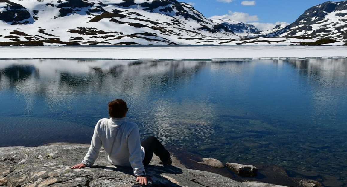 Frau sitzt am Ufer eines Sees in Norwegen.